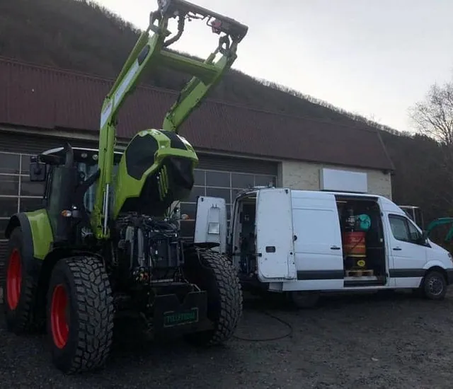 Traktor og servicebil står parkert utenfor verksted, klar for vedlikehold.