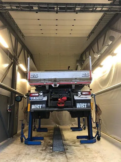 Lastebil hevet på løftebukk i stor hall for service og vedlikeholdsarbeid.