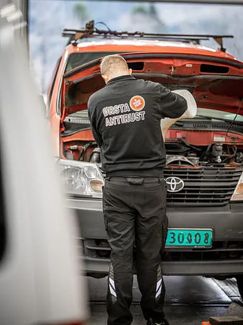Mekaniker fyller væske i en rød Toyota med panseret åpent i verkstedhall.